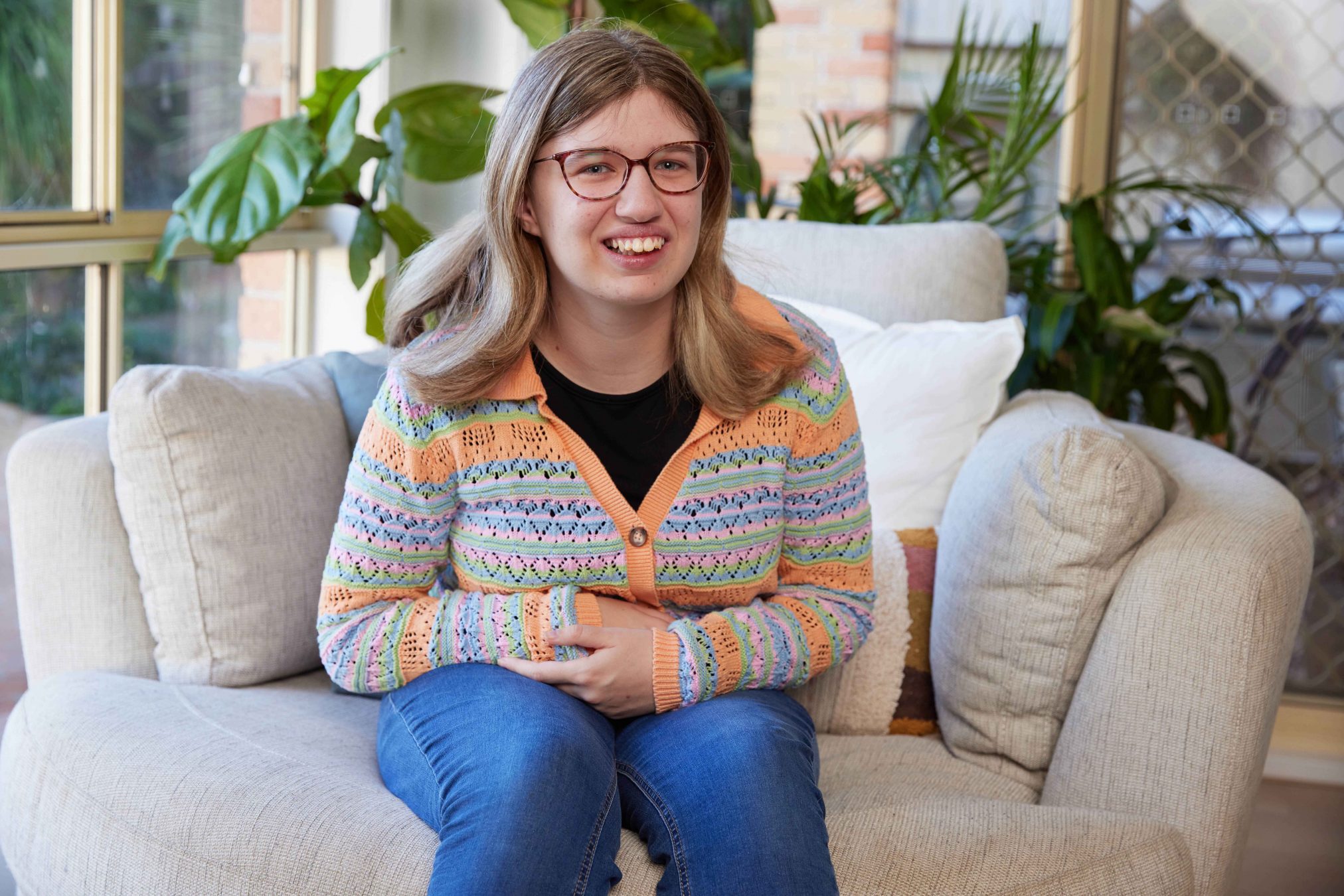 A young woman sitting on a lounge and smiling.