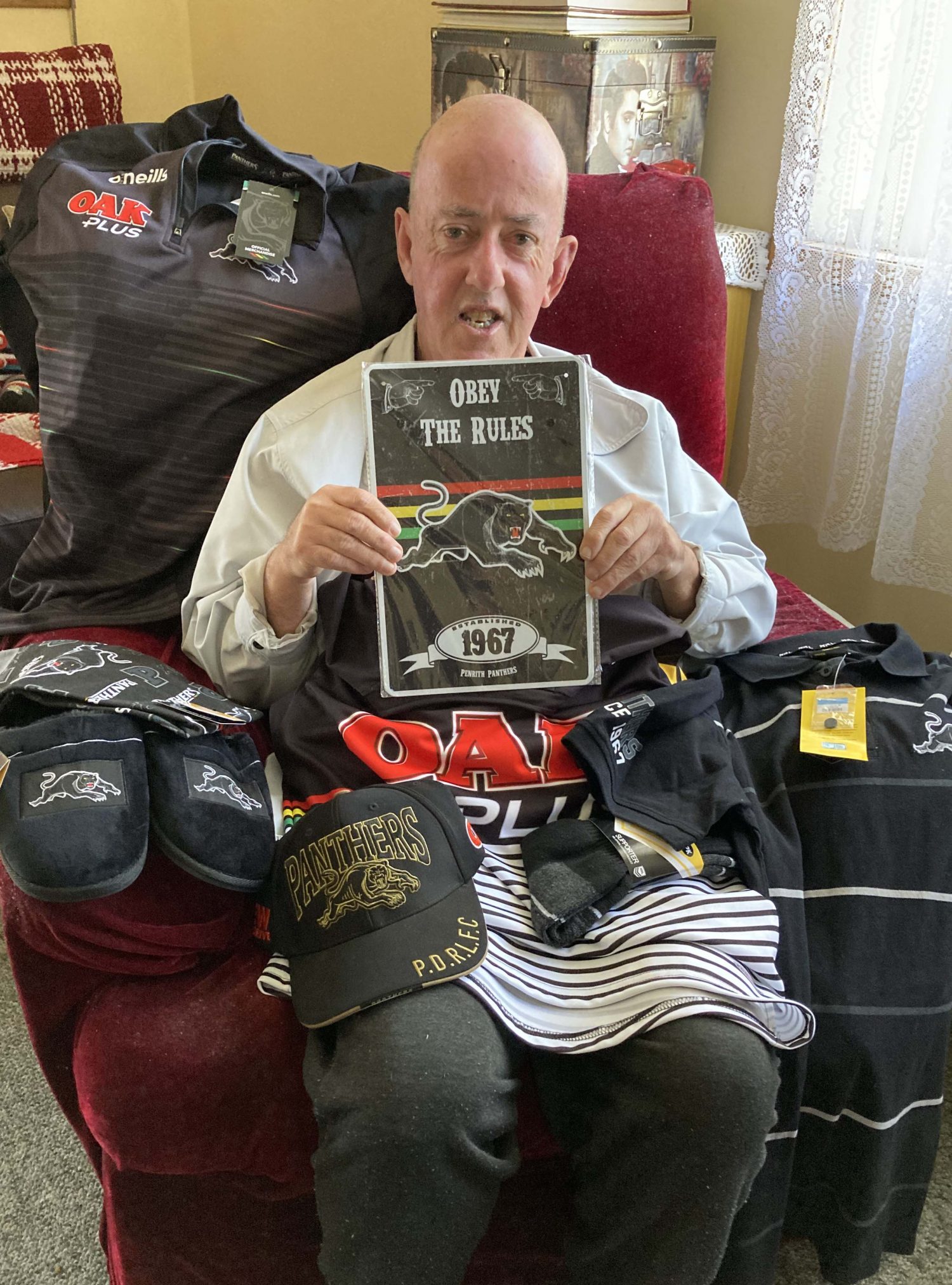 Brett surrounded by his new Panthers merchandise. He is sitting in a red armchair.