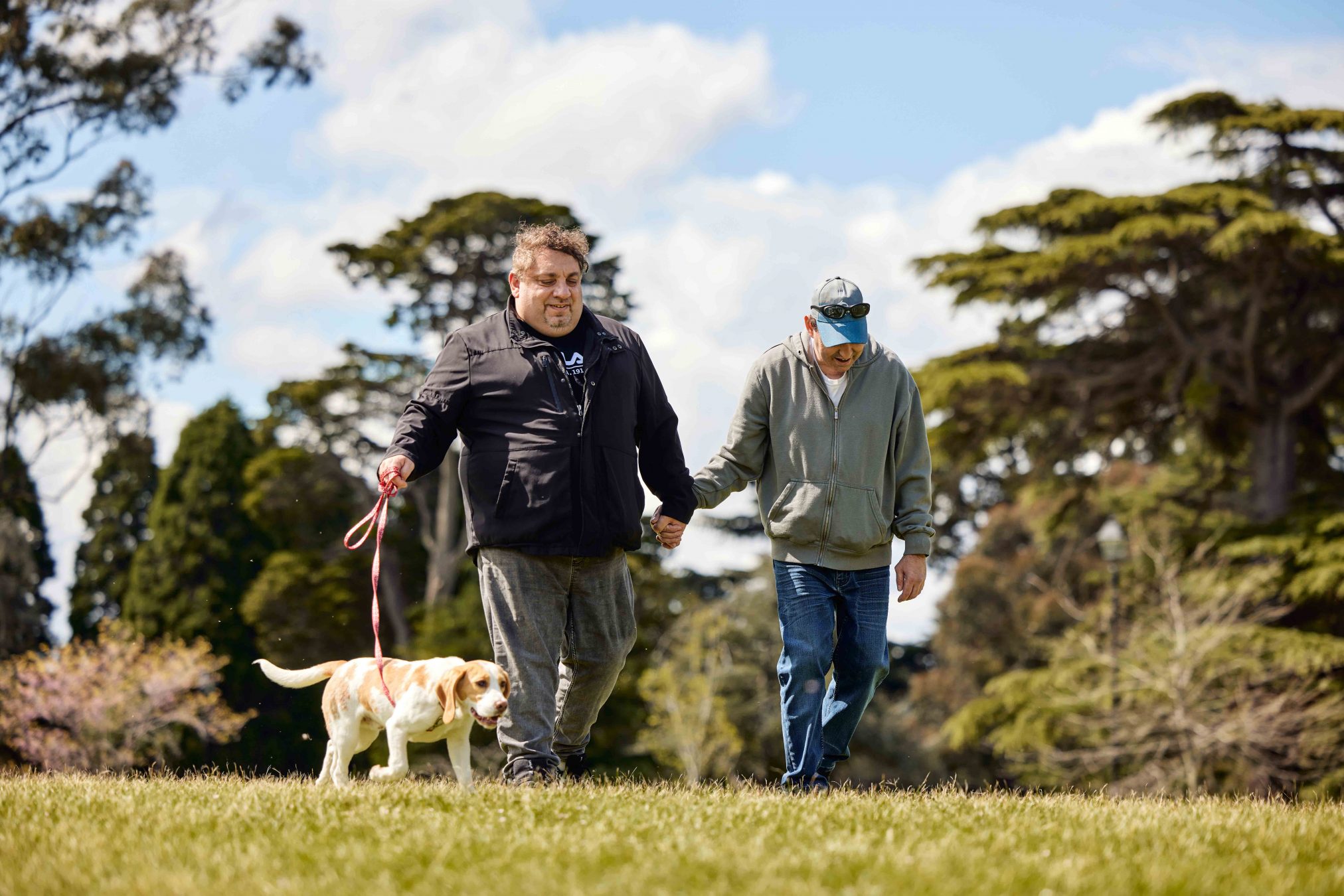 Client and Support Worker walking in park. The Support Worker is holding a dog on a leash.