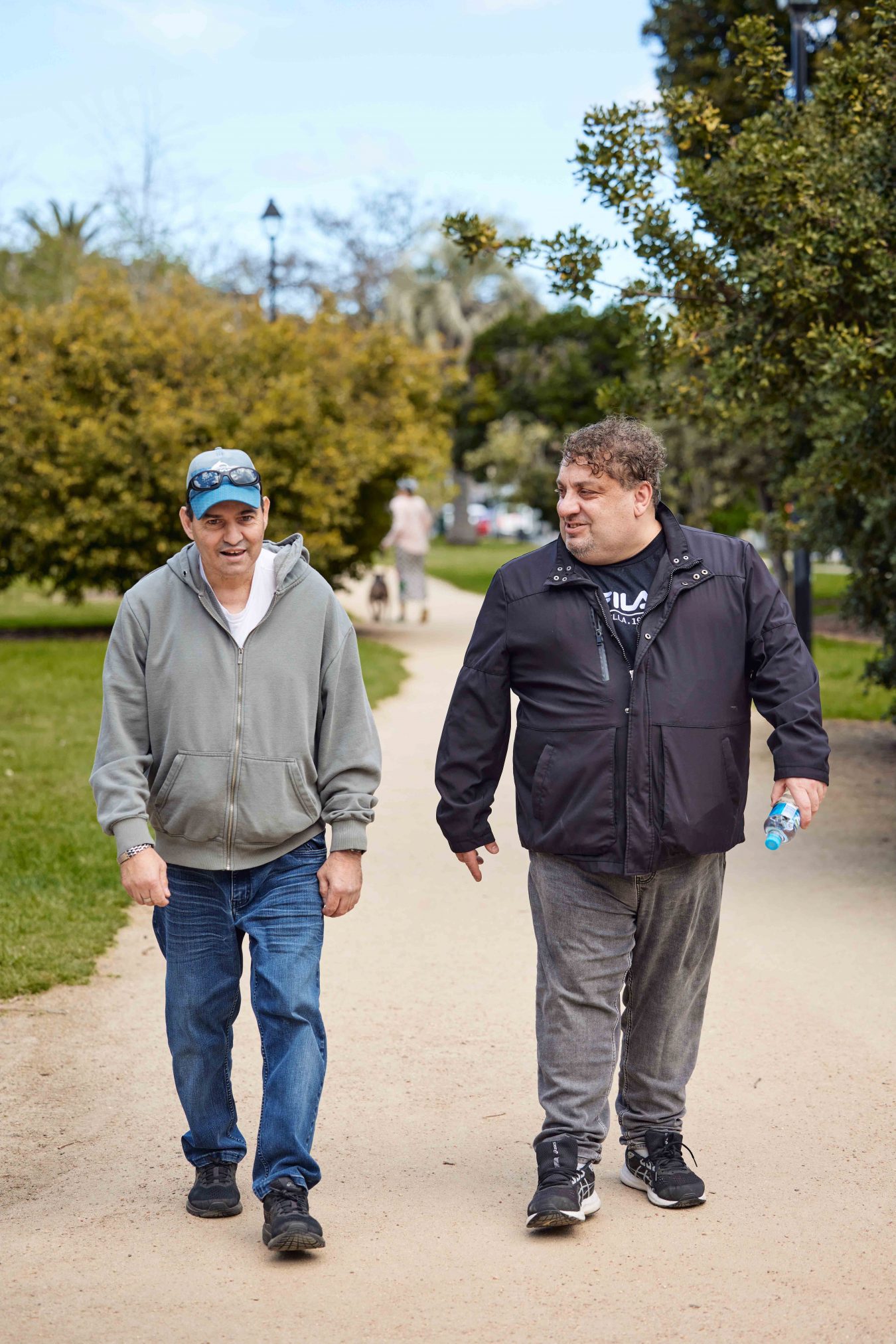 Support Worker and Client walking on foot path in park. Support Worker is smiling at client.