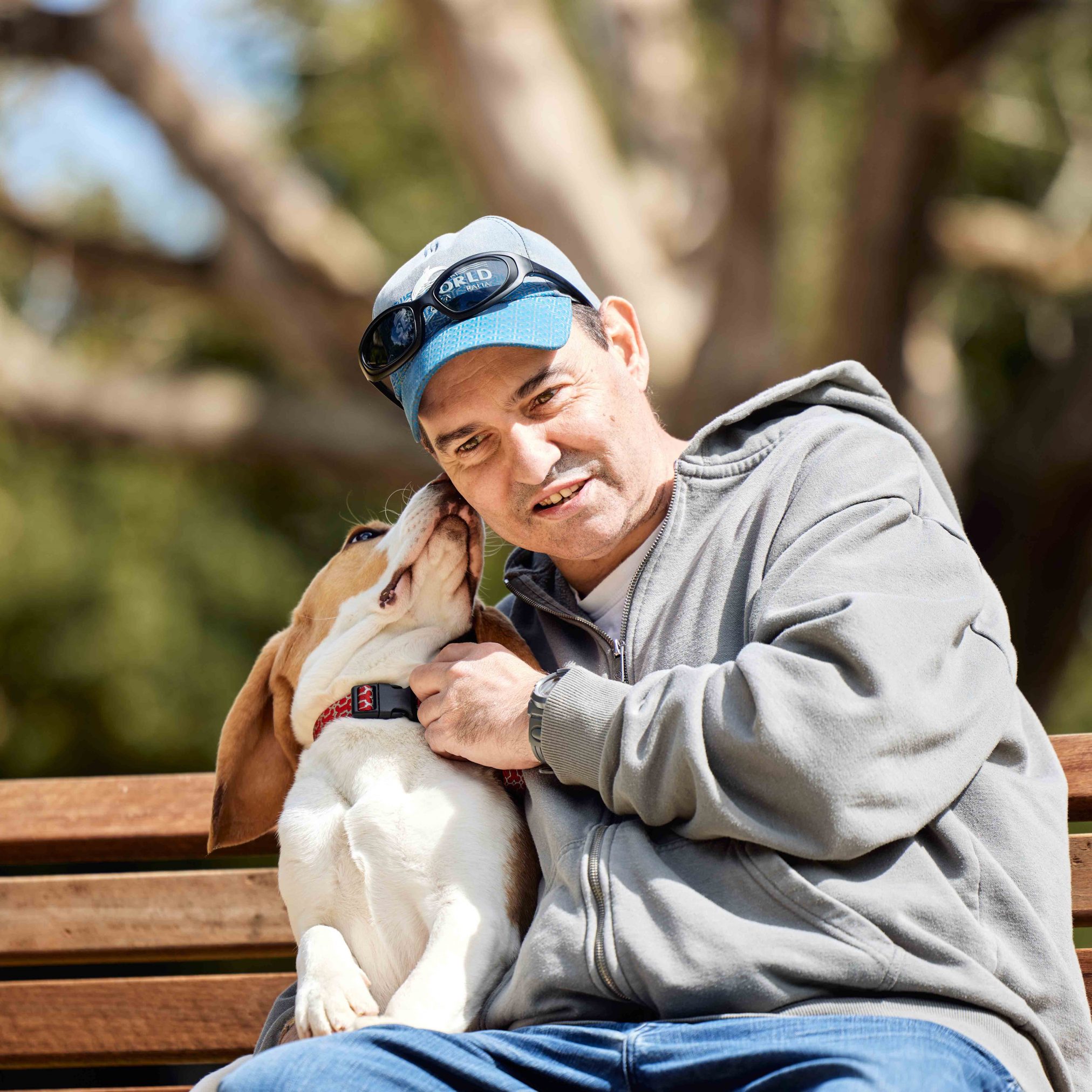 Dog is licking client's cheek while they sit on park bench.