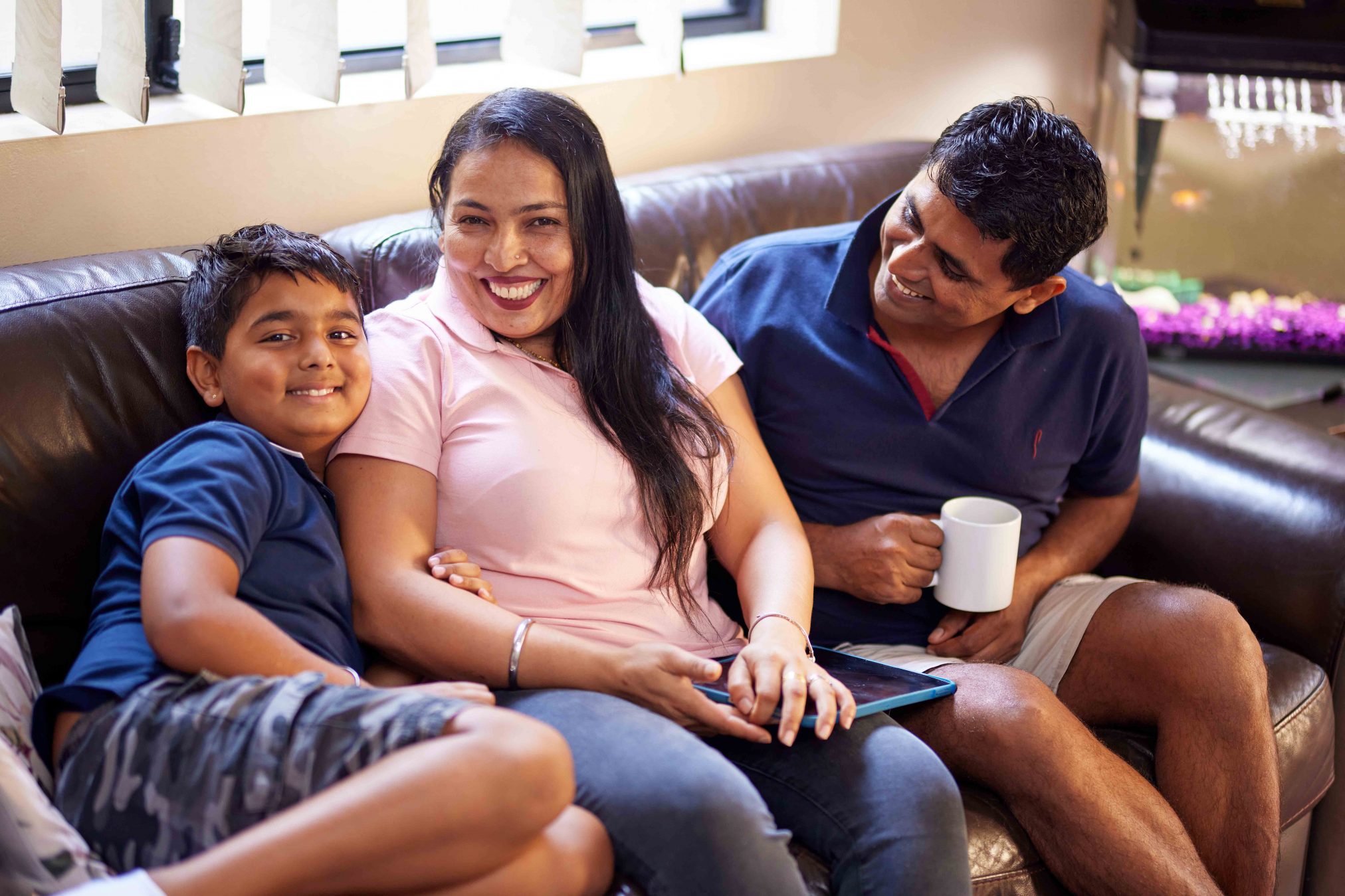 Parents sitting on a couch with their son, everyone is smiling.