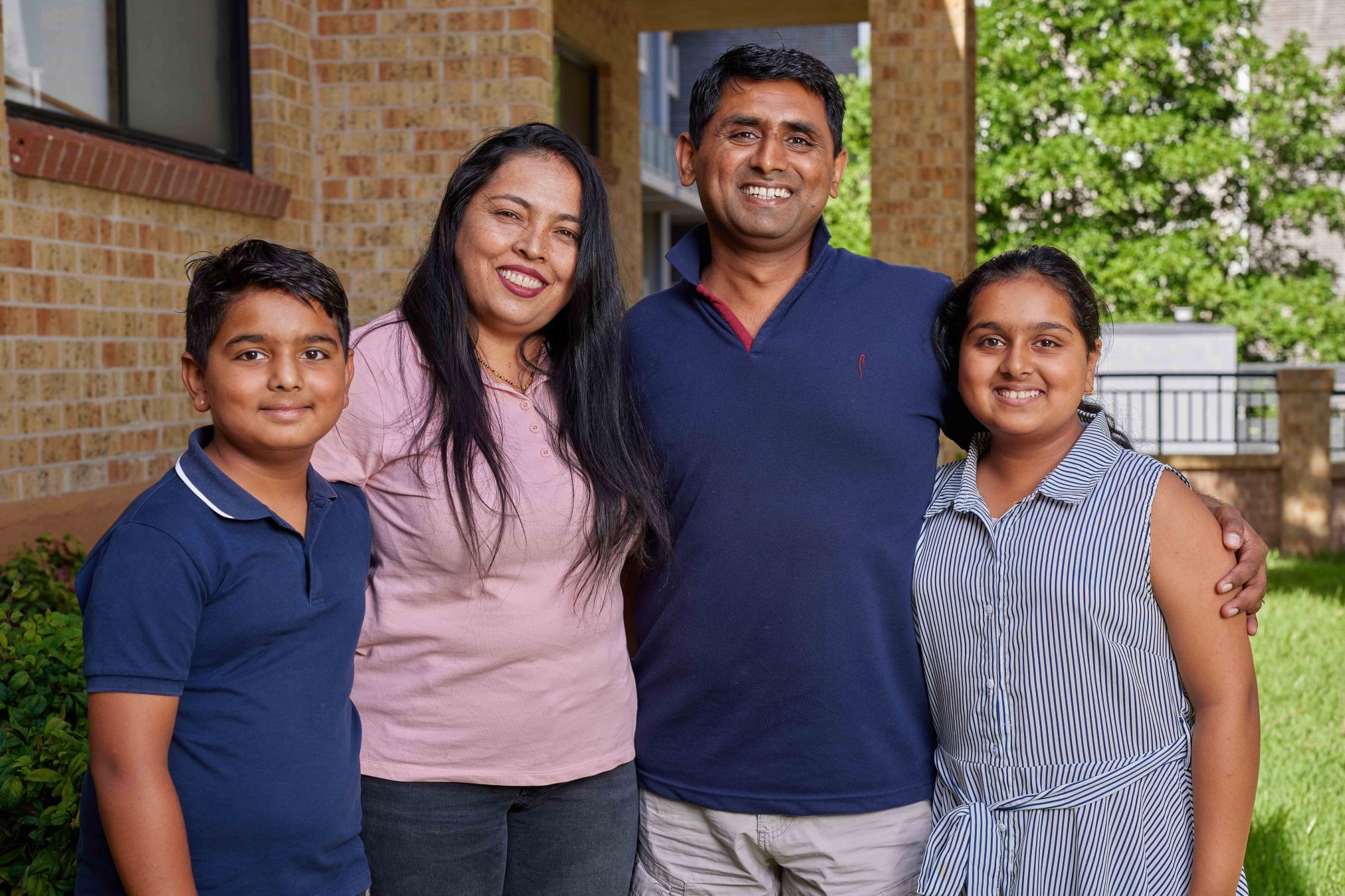 a family portrait - four people standing outside, a leafy tree in the background