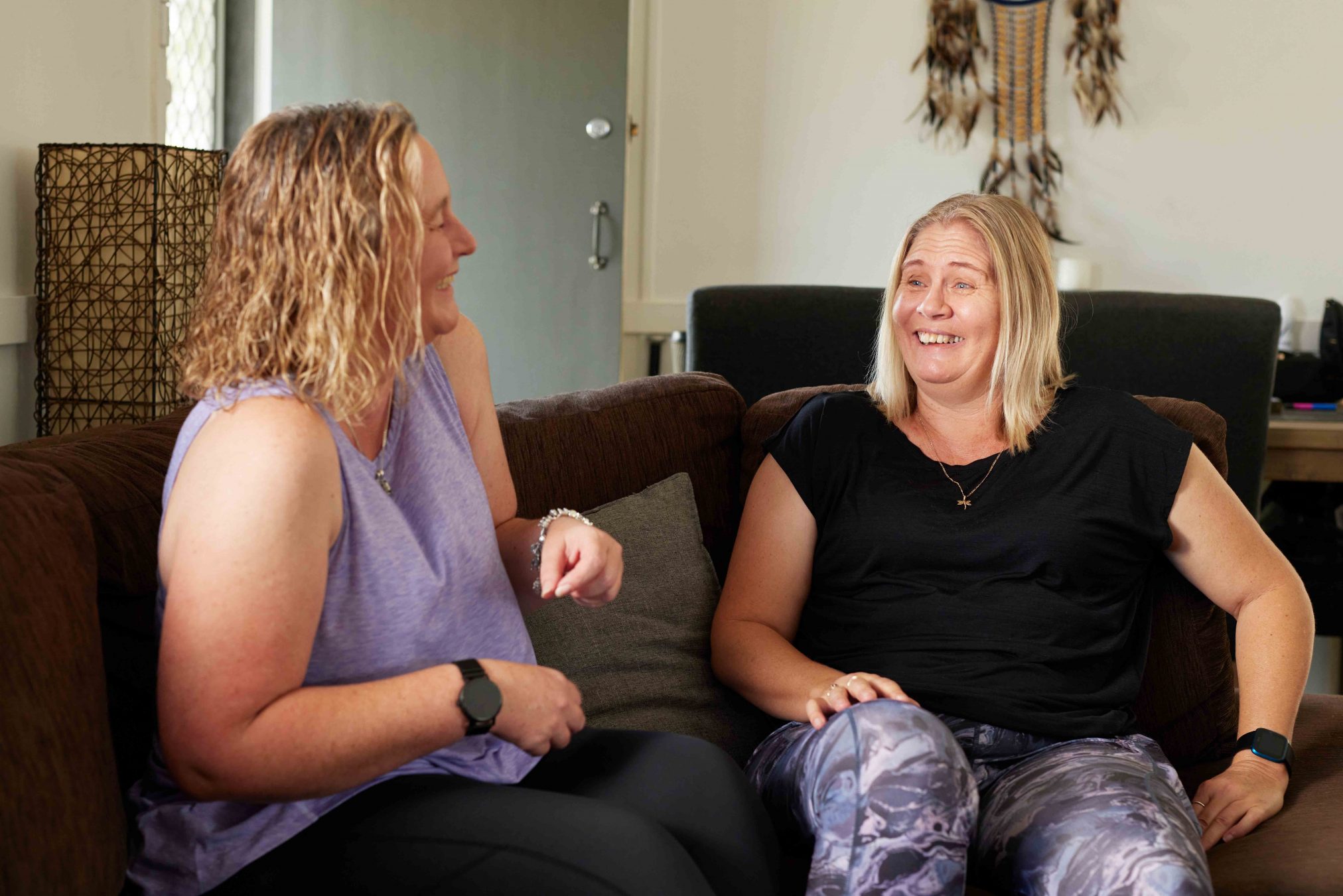 Two women laughing while sitting inside on a lounge.