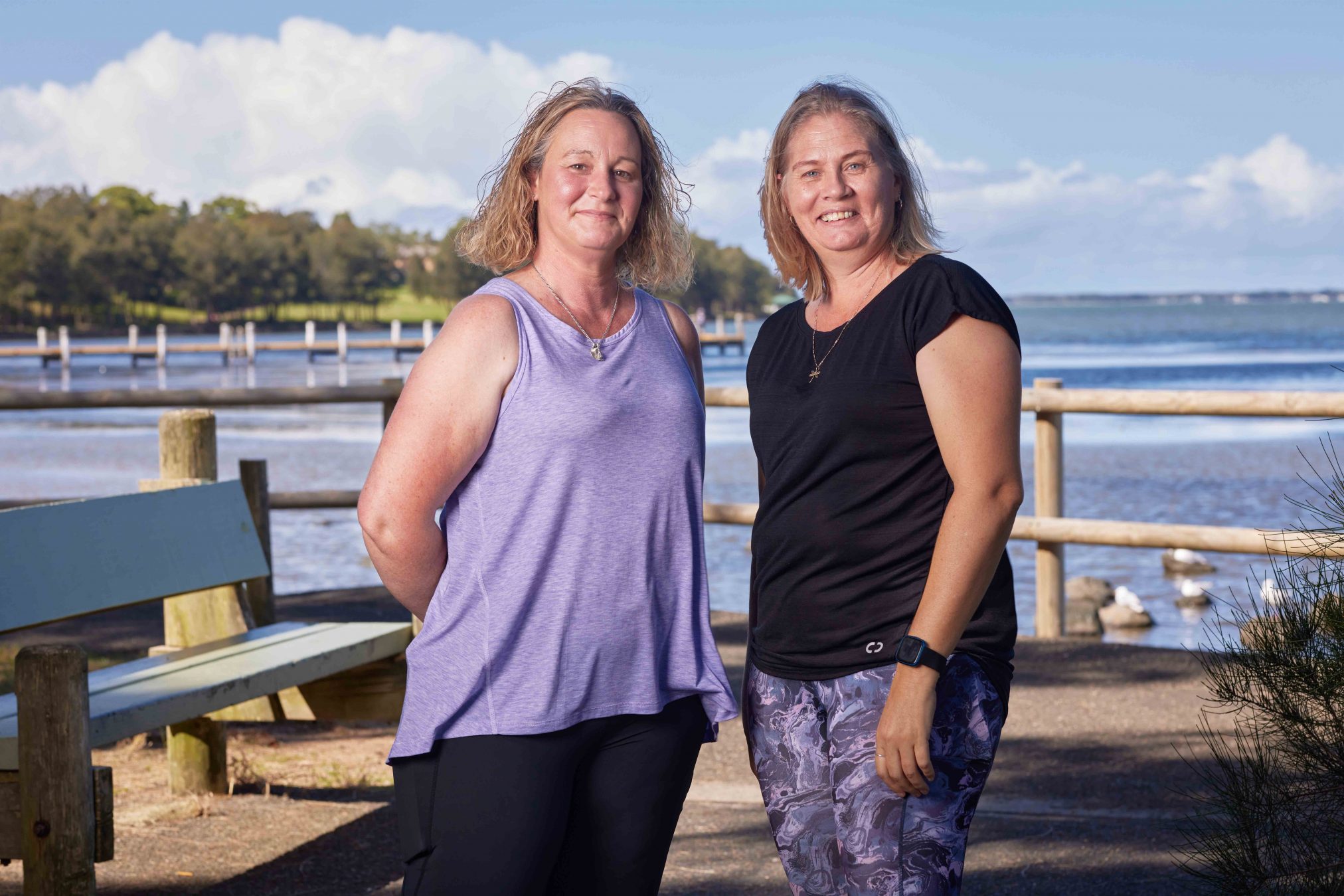 Two women smiling at the camera with a lake in the background.