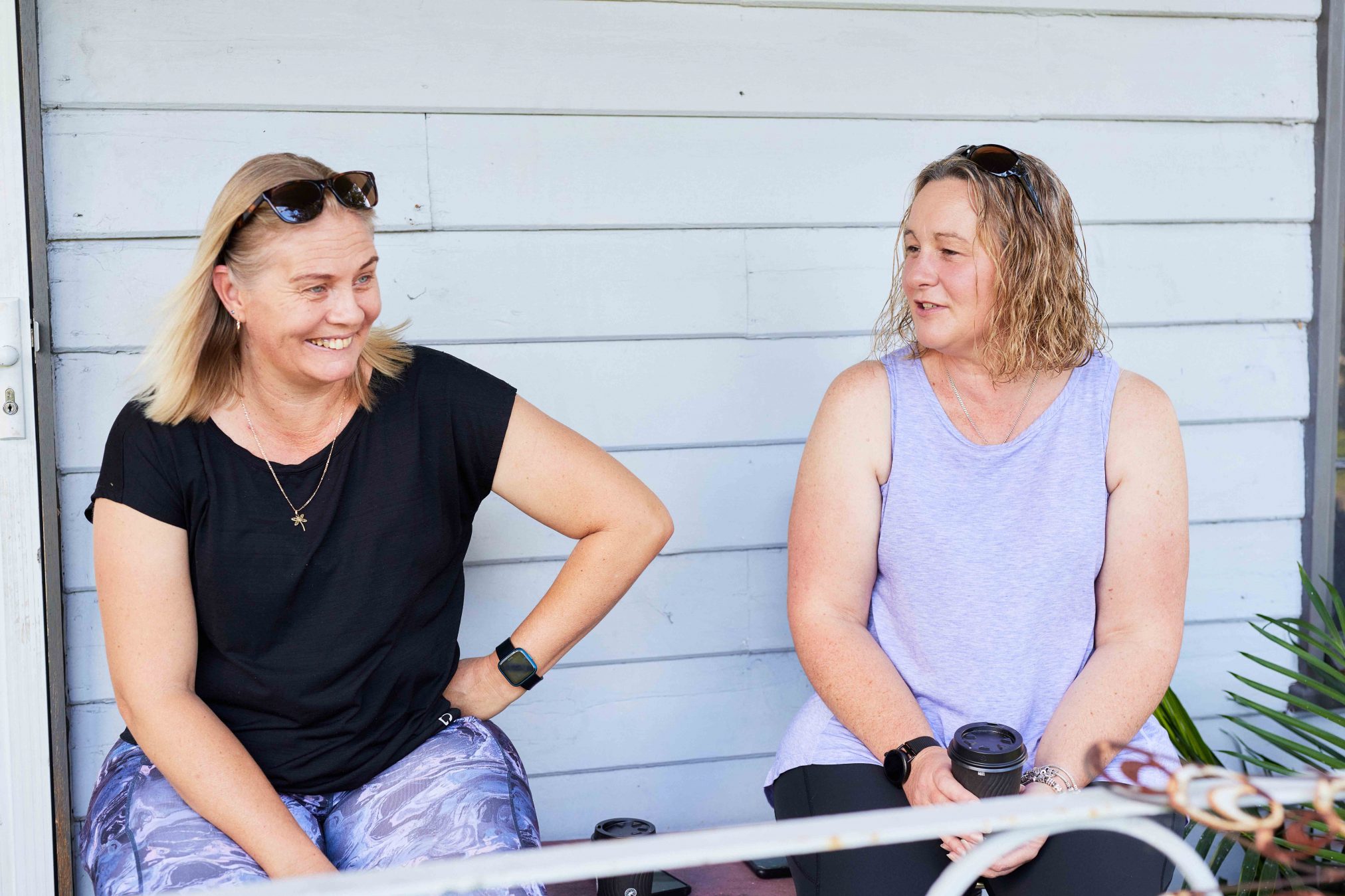 Two women having a conversation. One is laughing and they are sitting on a veranda.