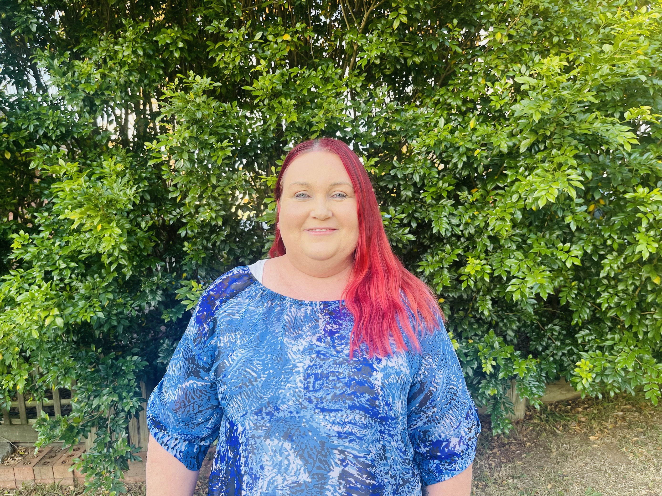 Woman in a blue top and red hair smiling at camera.